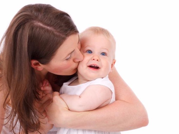 Parent kissing a smiling baby on the cheek against a white background.